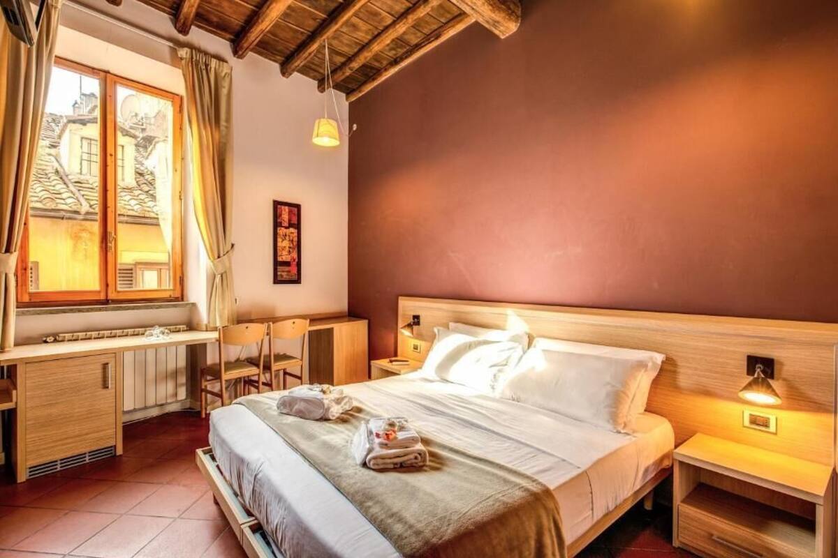 A hotel room with a bed, bedside tables, a desk, and a window with curtains.