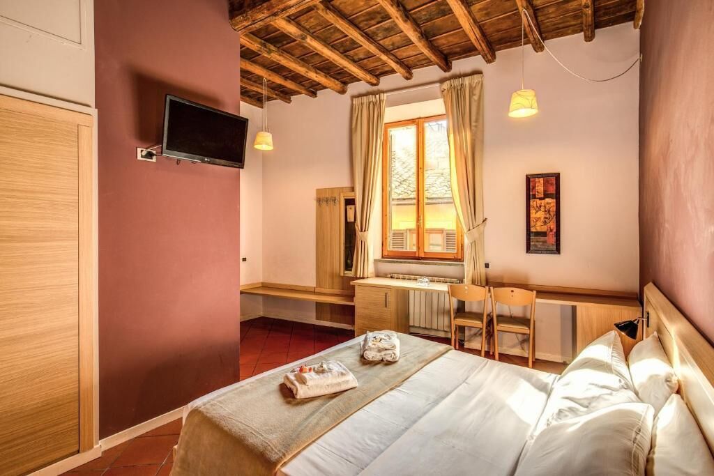 A bedroom with a bed, a desk, a chair, a TV, and a window with curtains.