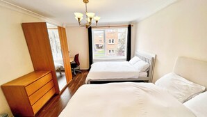 Une chambre d’hôtel avec deux lits, une commode en bois, une chaise et une grande fenêtre donnant sur des immeubles.