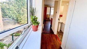 Un couloir avec un pot de fleurs, une fenêtre et une vue sur les arbres à l’extérieur.