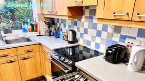 Une cuisine avec des meubles de rangement en bois, une cuisinière, une machine à café et un égouttoir à vaisselle.