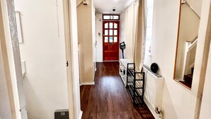 Un couloir avec un plancher en bois, une porte rouge et un radiateur fixé au mur.