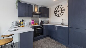 Een moderne keuken met donkerblauwe kastjes, een wit aanrecht, een inbouwoven, een magnetron en een grote wandklok.