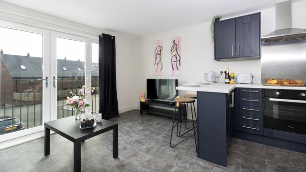 Een moderne keuken met donkere kasten, een inbouwoven en een eethoek met een tafel en stoelen.
