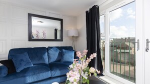 Een woonkamer met een blauwe bank, een spiegel, een lamp en uitzicht door een glazen deur.
