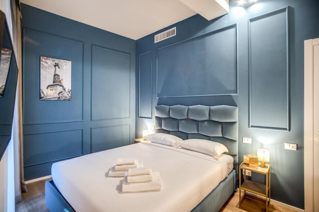 Une chambre à coucher avec un grand lit, une tête de lit à motifs capitonnés et une petite table de chevet avec une lampe.