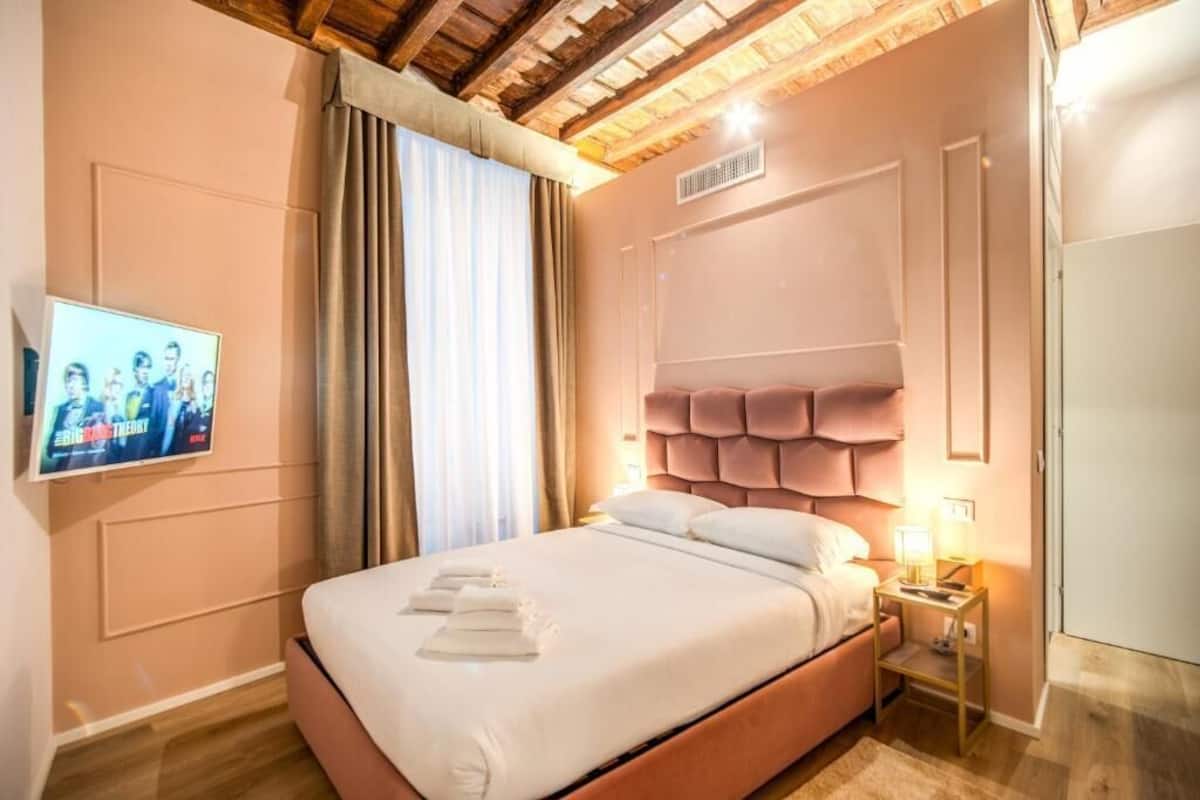A bedroom with a bed, a television, a nightstand, and a window with curtains.
