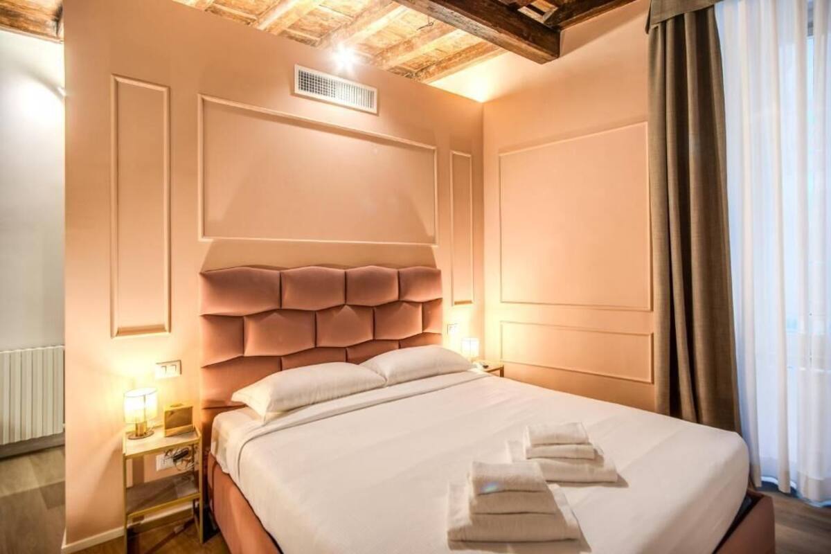 A hotel room with a large bed, a nightstand with a lamp, and a wooden ceiling.