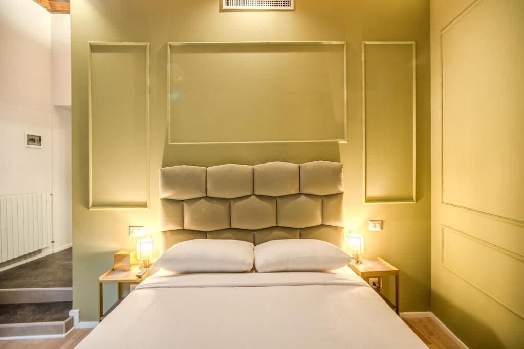 Un dormitorio con una cama grande, dos mesitas de noche con lámparas, un cabecero y una escalera.