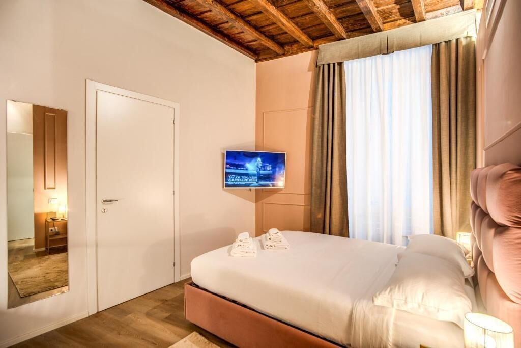 A bedroom with a bed, a television mounted on the wall, a door, and a window with curtains.