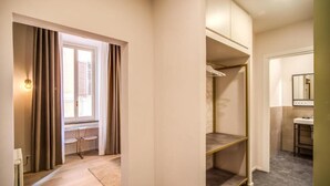 Et hotelværelse med walk-in-skab, et vindue med gardiner, en radiator og et badeværelse med håndvask og spejl.