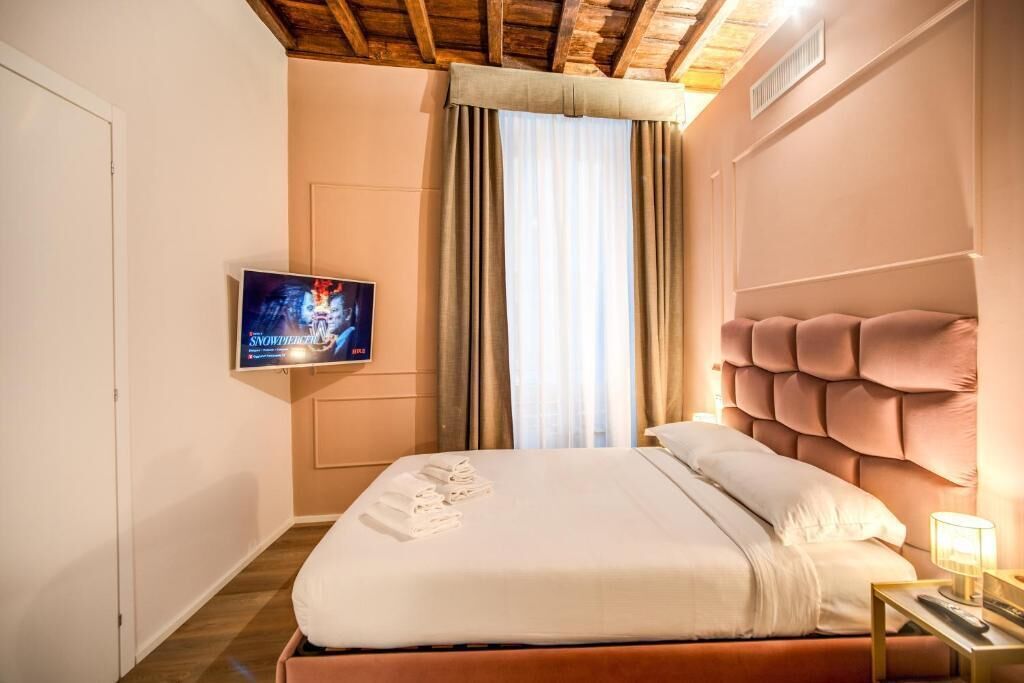 Habitación de hotel con cama, televisión montada en la pared y ventana con cortinas.