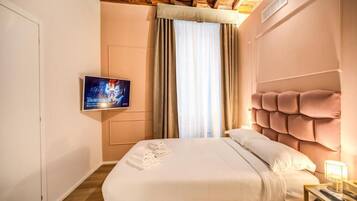 Habitación de hotel con cama, televisión montada en la pared y ventana con cortinas.
