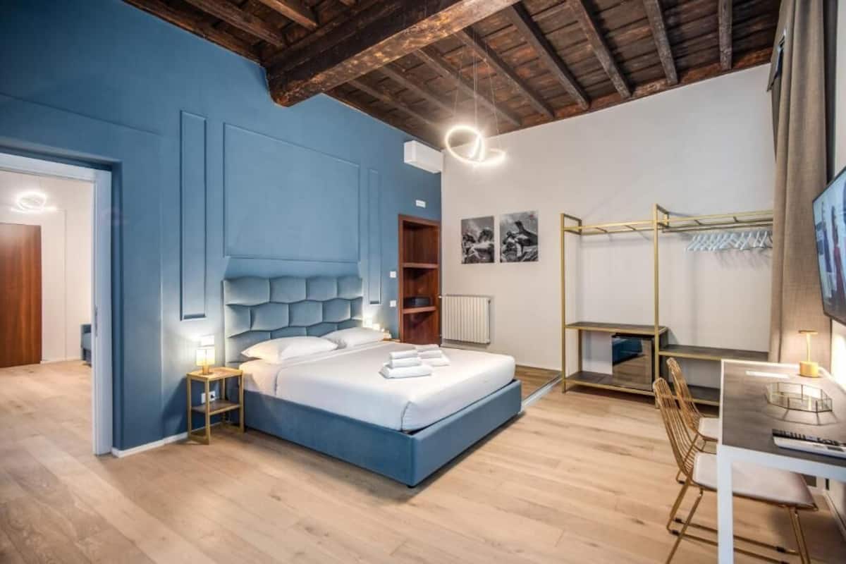 A bedroom with a large bed, a desk with a chair, a TV, and a wardrobe.