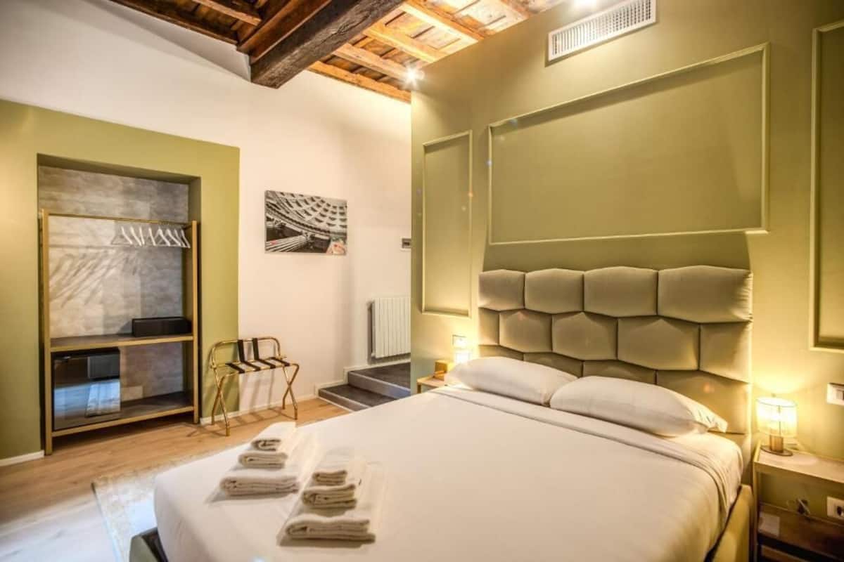 A hotel room with a bed, a seating area with a chair, a small table, and a wall-mounted shelf.