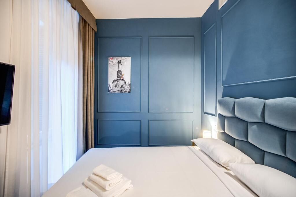 A hotel room with a large bed, a blue accent wall, and a framed picture of a building.