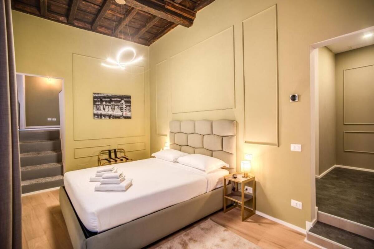 A hotel room with a bed, a nightstand, a wall-mounted light, and a staircase.