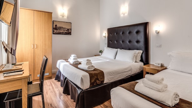 A hotel room with a large bed, a desk with a chair, a wardrobe, and a bedside table with a lamp. - Magenta Collection Cancello (Rome)