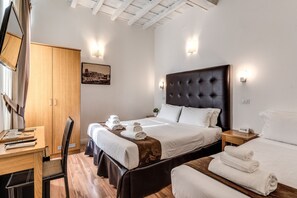 A hotel room with a large bed, a desk with a chair, a wardrobe, and a bedside table with a lamp.