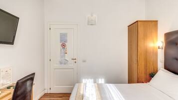Habitación de hotel con cama, escritorio y silla, armario, televisor y puerta con un aviso.