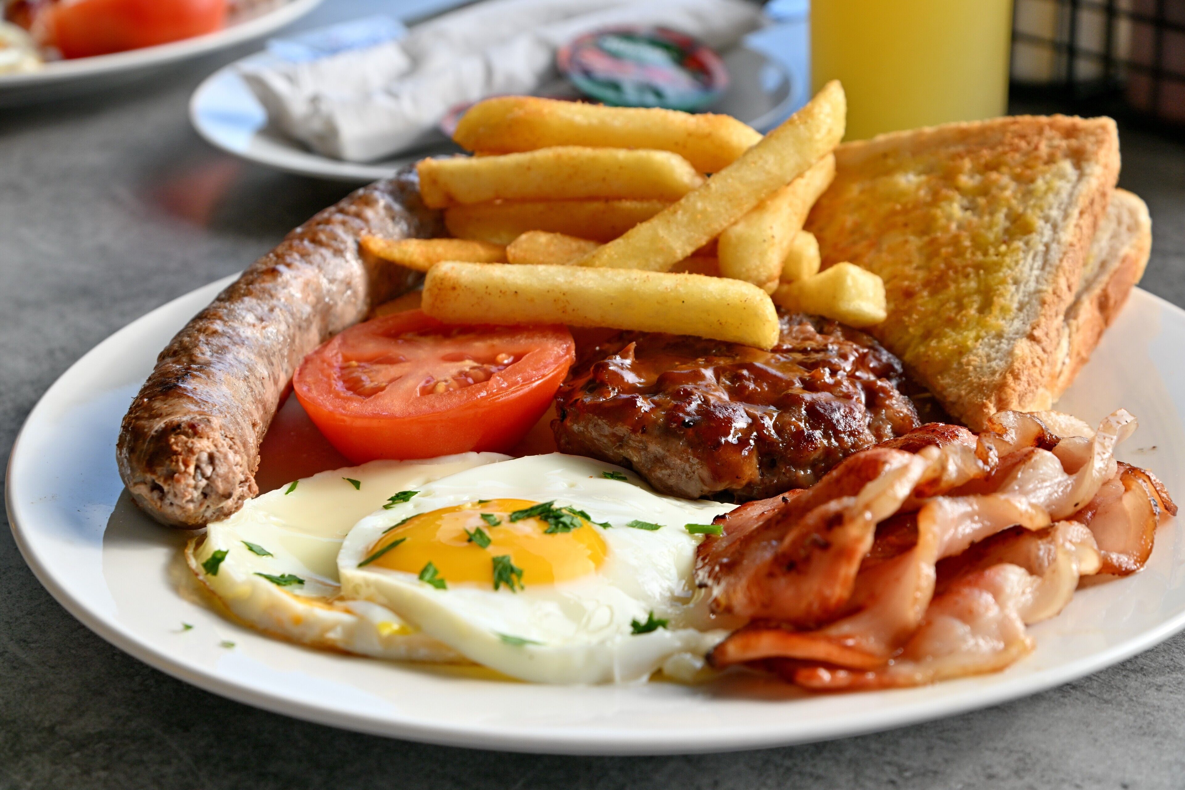 A plate of breakfast food including sausages, eggs, bacon, toast, and fries.