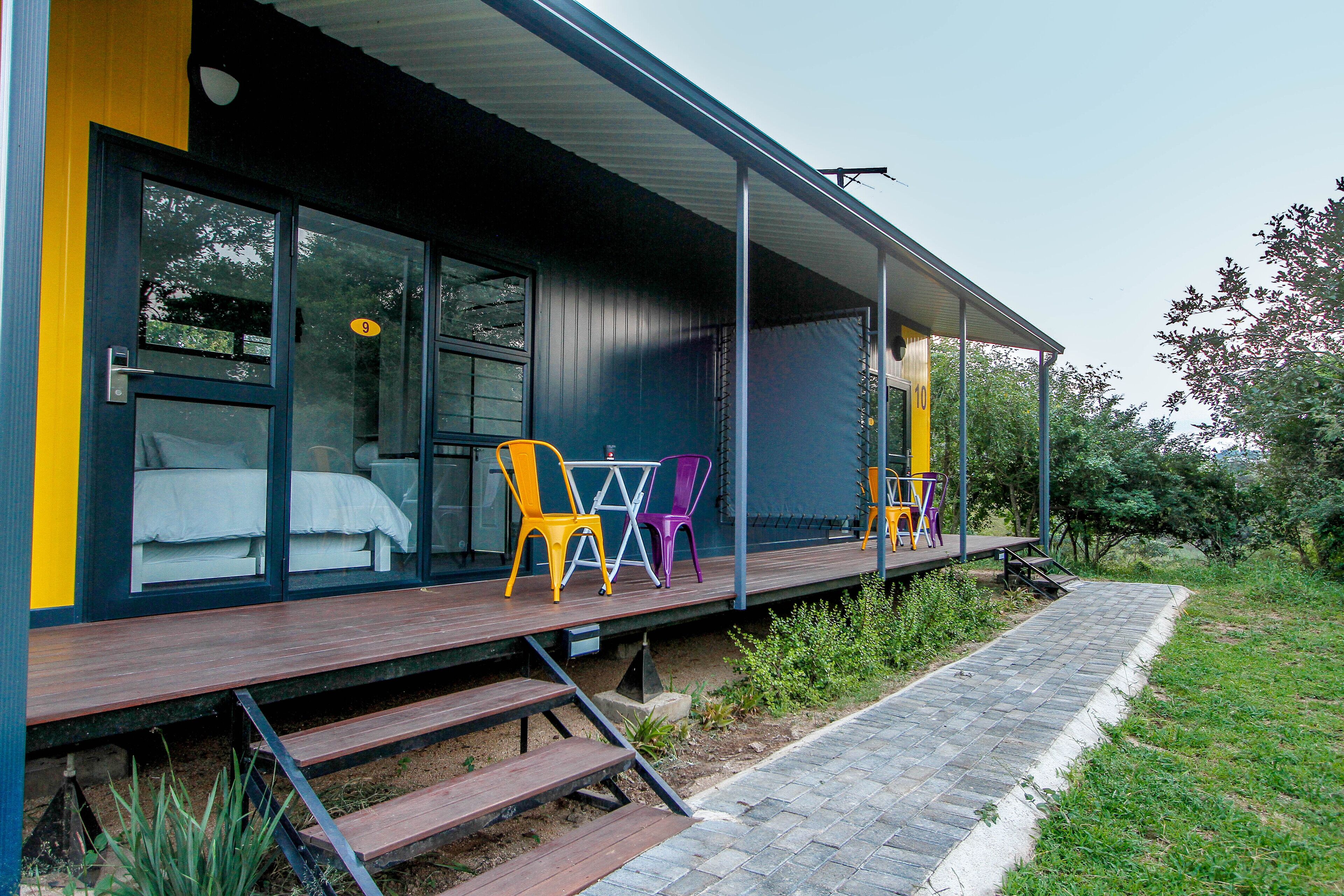 A modern house with a wooden deck, a covered porch, and a small outdoor seating area with colorful chairs.