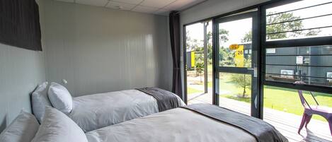 A modern hotel room with two beds, a large window, and a view of the outside.