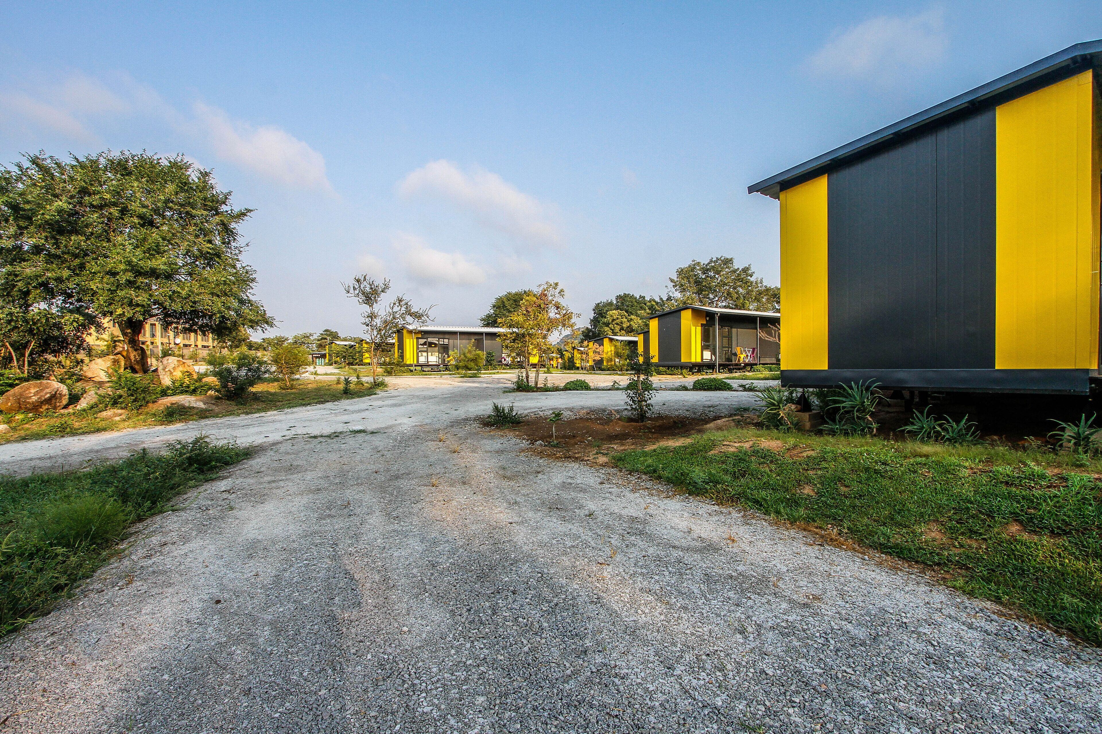 A gravel road leading to a row of modern, yellow and black buildings with a natural landscape on either side.
