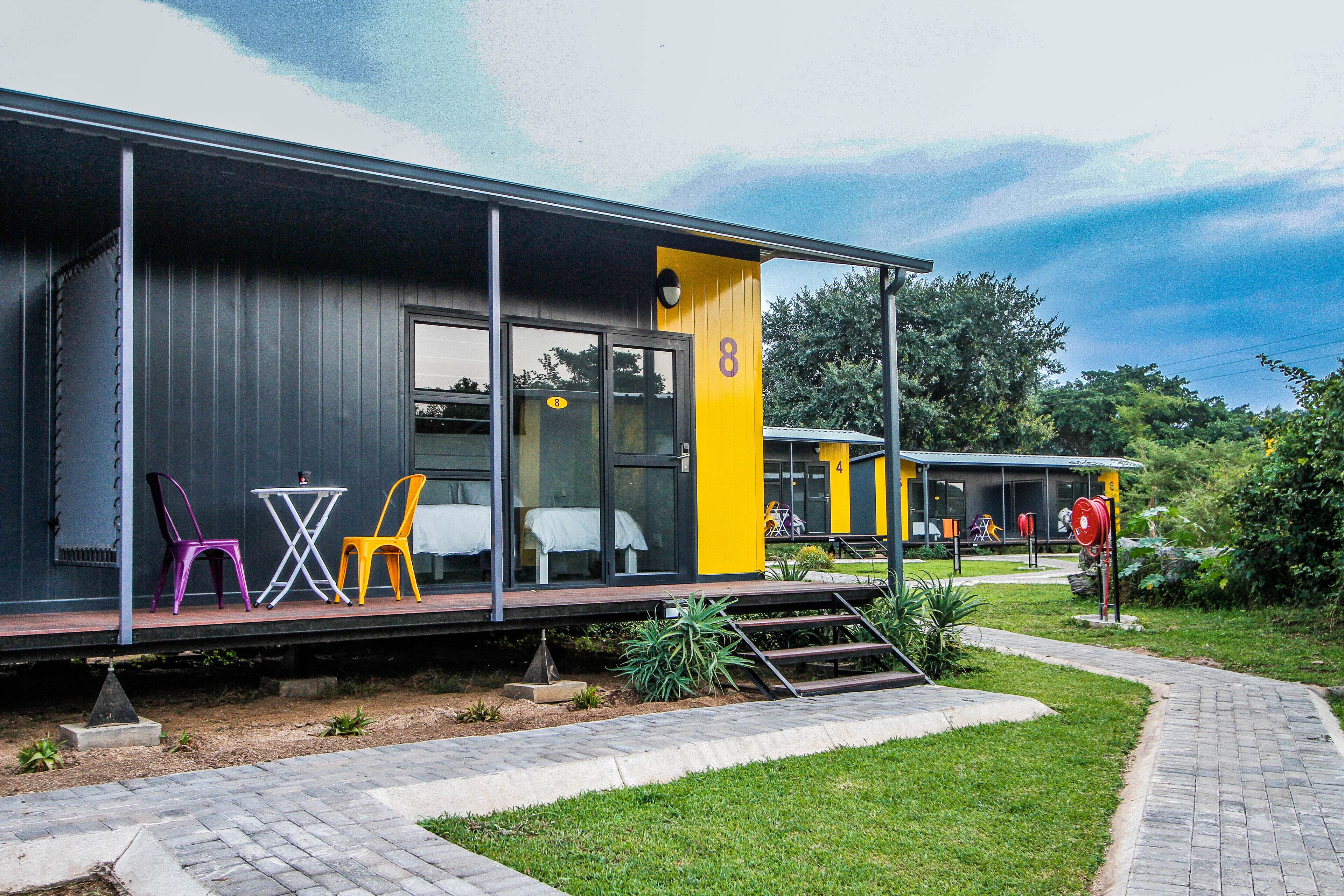 Un bâtiment moderne à la façade jaune et noire, doté d’un espace extérieur abrité avec des chaises colorées et une petite table.