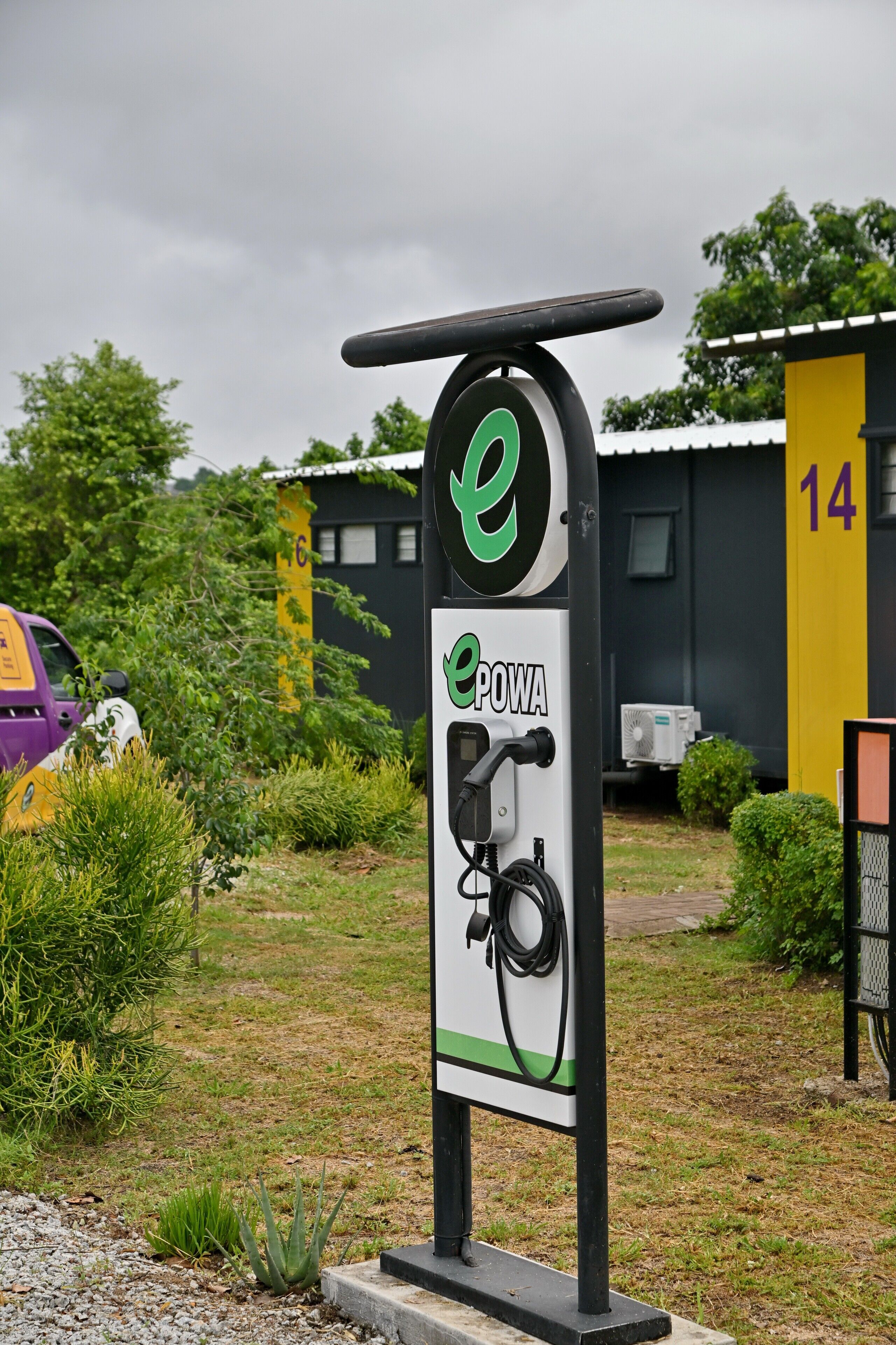An electric vehicle charging station with a sign labeled "ePOWA" in a grassy area with a building in the background.