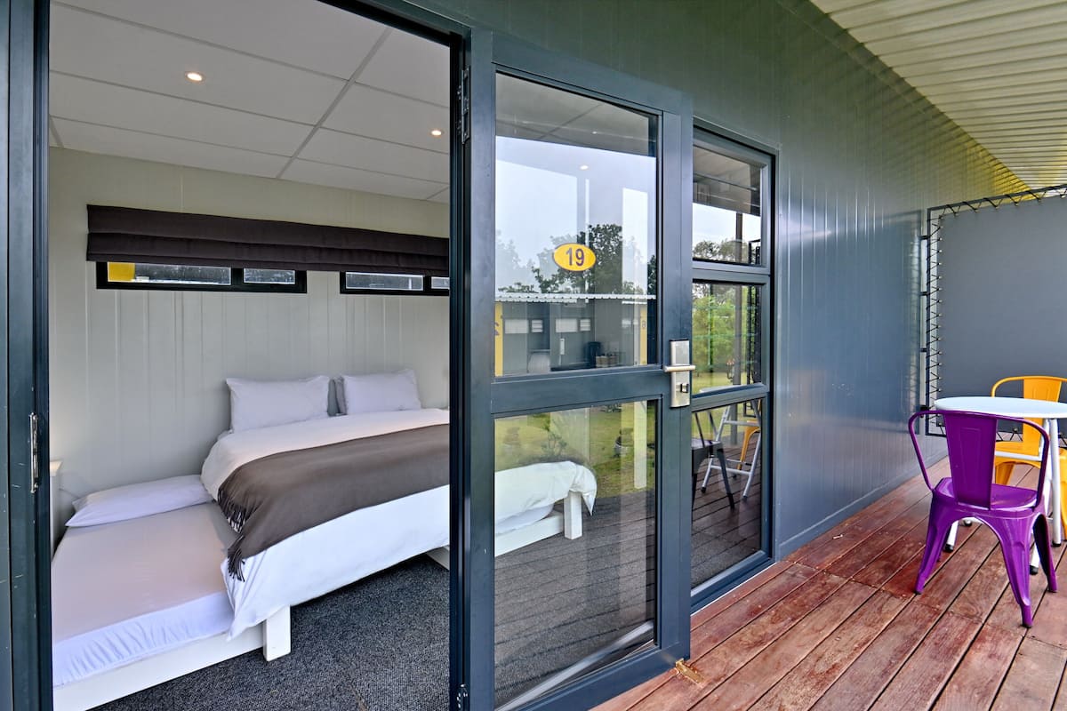 Ein Zimmer mit einem Bett, einem Fenster mit der Nummer 19 und einer Terrasse mit Tisch und Stühlen.