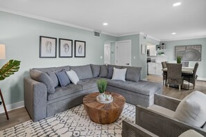Un salon avec un canapé d’angle gris, une table basse ronde en bois et un tapis à motifs.