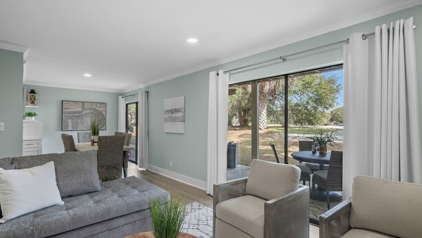 Una sala de estar moderna con un sofá gris, sillones color beige y una zona de comedor con mobiliario de mimbre.