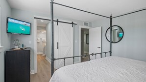 Un dormitorio con cama con dosel, un televisor en la pared y un espejo con marco perlado.