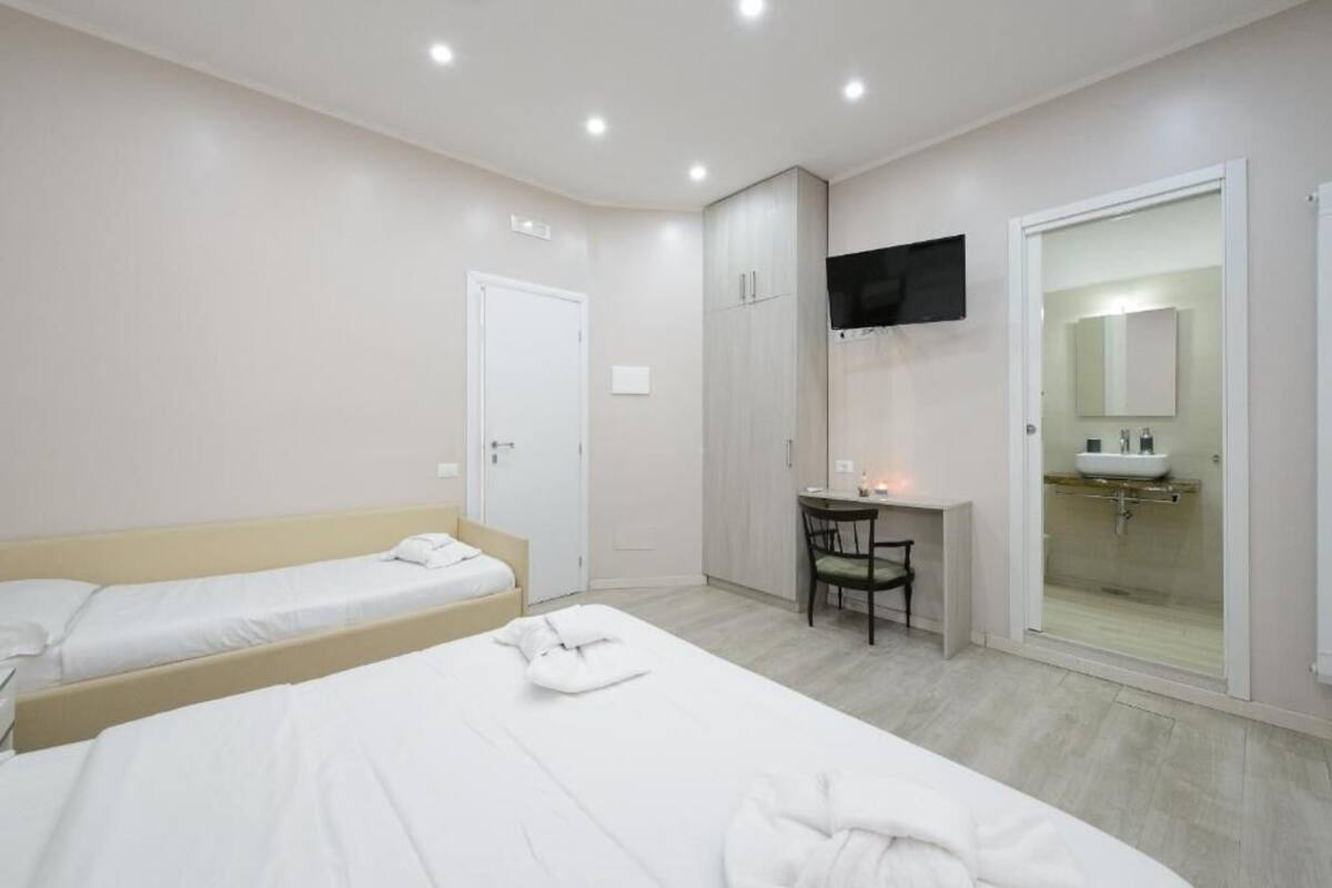 A hotel room with two beds, a desk, a chair, a TV, and a bathroom with a glass shower enclosure.
