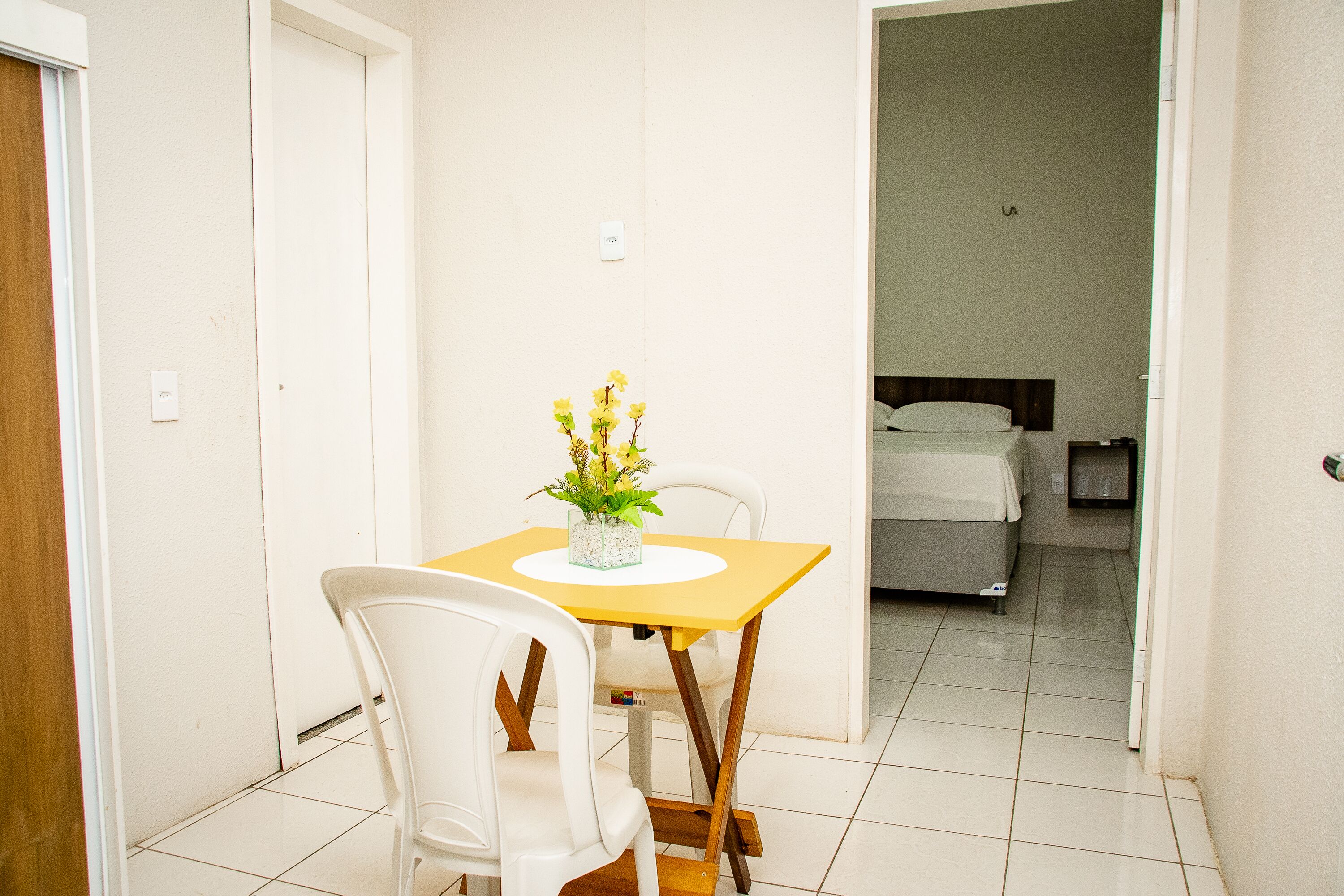 A small, clean room with a bed, a table with chairs, and a vase of flowers.