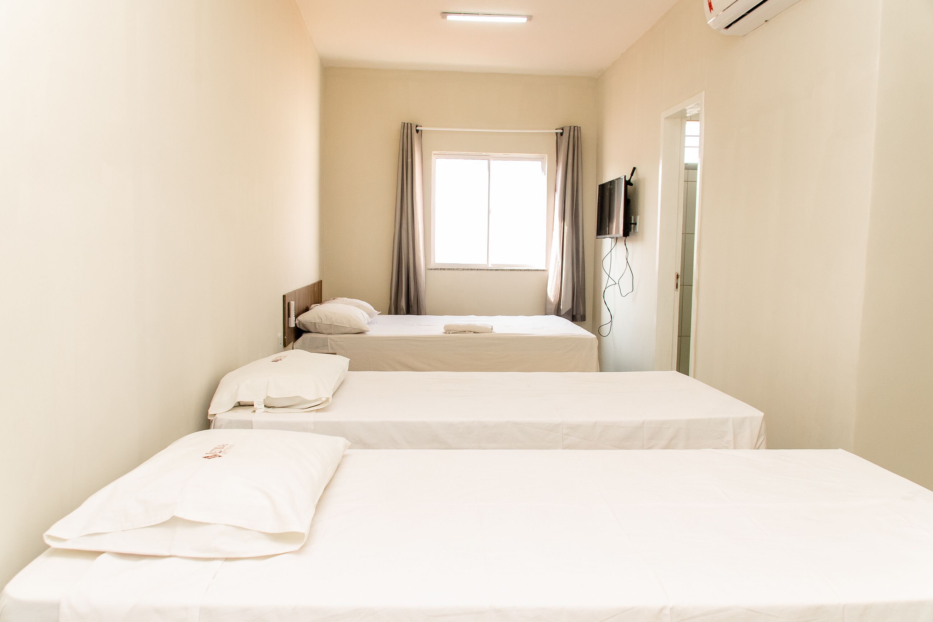 A hotel room with two beds, a window with curtains, a flat-screen TV mounted on the wall, and a door.