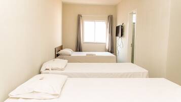 A hotel room with two beds, a window with curtains, a flat-screen TV mounted on the wall, and a door.