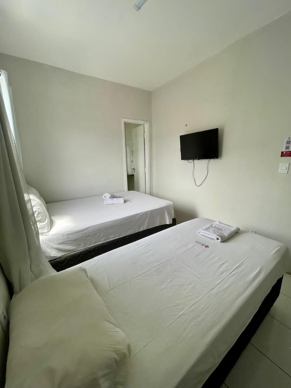 A hotel room with two beds, a flat-screen TV mounted on the wall, and a door leading to a bathroom.
