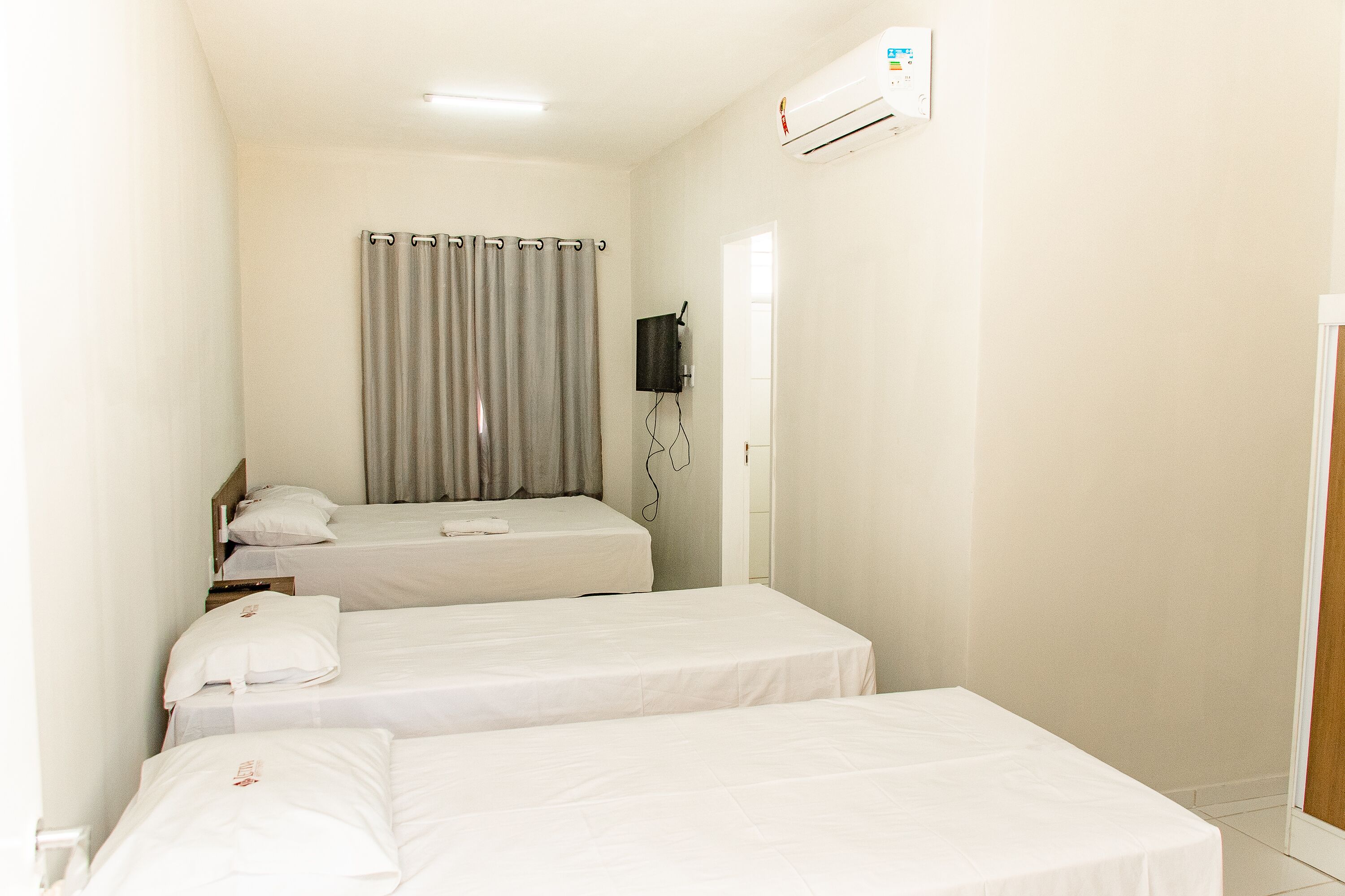 Ein Hotelzimmer mit zwei Einzelbetten, einem grauen Vorhang, einem Wand-Fernseher und einer Klimaanlage.