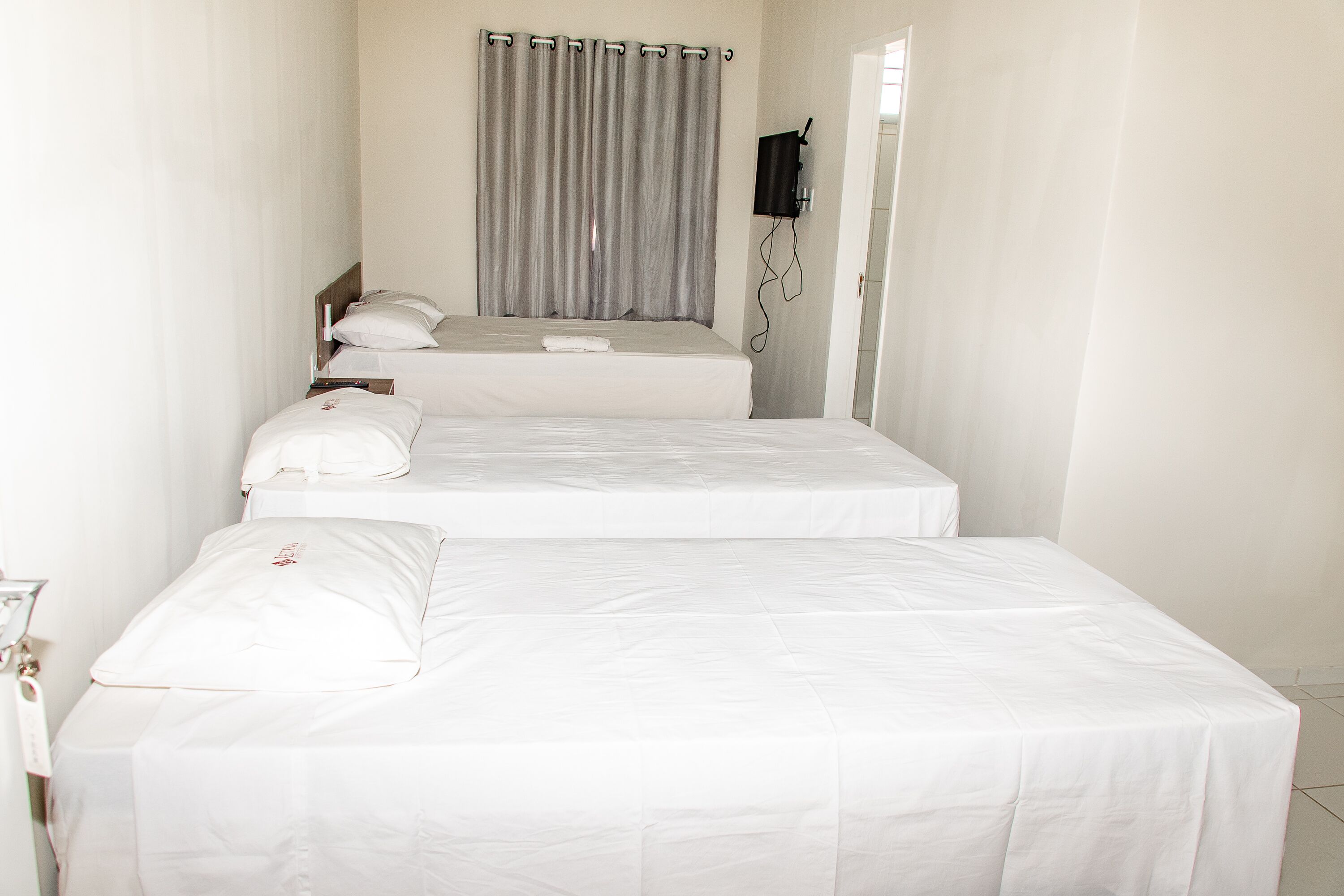 Een hotelkamer met twee enkele bedden, een aan de muur bevestigde televisie en een gordijn.