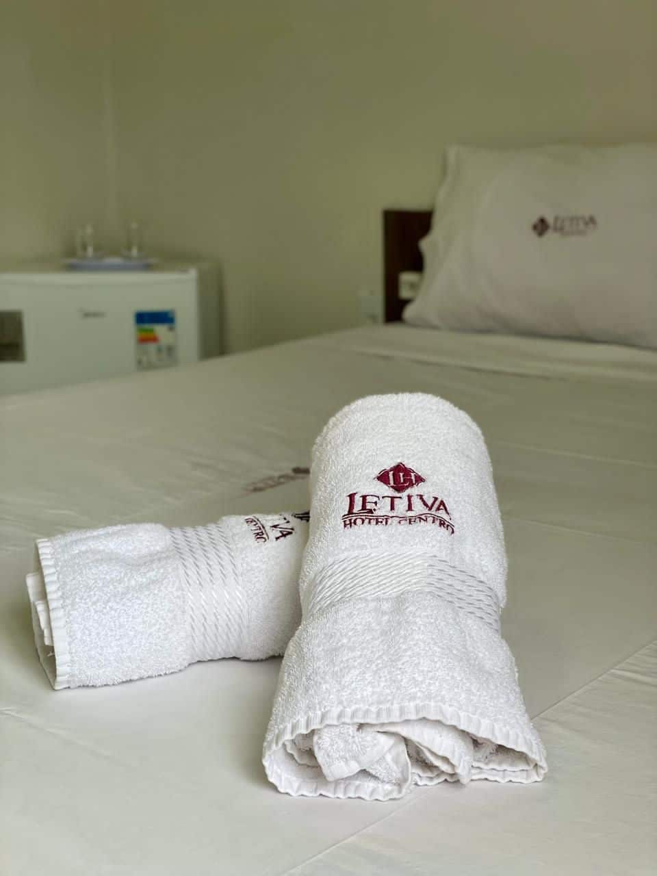 A neatly made bed with a folded towel and a pillow with the logo "I'FIVA HOTEL CENTRE".