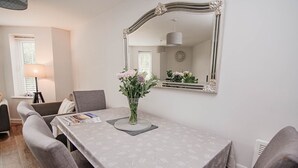 Un coin repas avec une table dressée pour quatre personnes, un vase rempli de fleurs et un grand miroir accroché au mur.