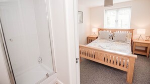 Une chambre à coucher avec un lit en bois, des tables de chevet, une fenêtre et un espace douche.