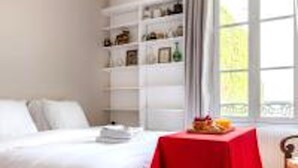 A bedroom with a bed, a red table, and a window with curtains. - Eiffel Tower Lourmel Residence  (Paris)