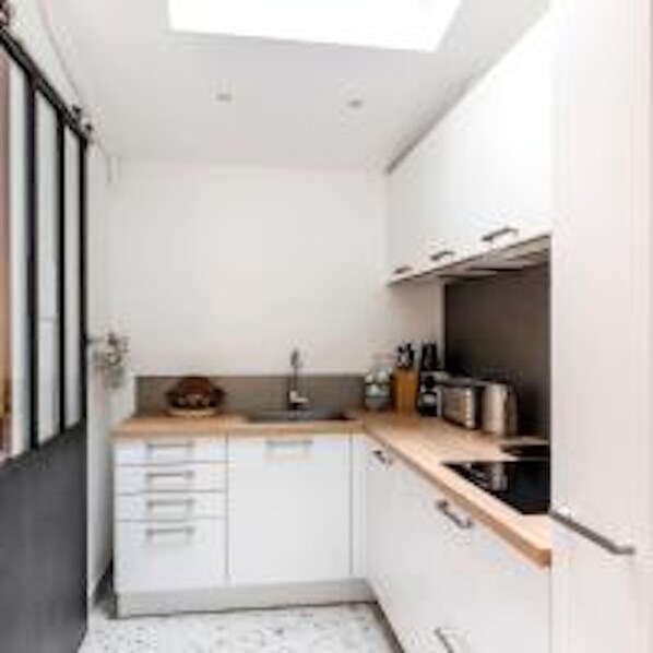 A compact kitchen with white cabinets, a wooden countertop, and a skylight. - Eiffel Tower Lourmel Residence (Paris)