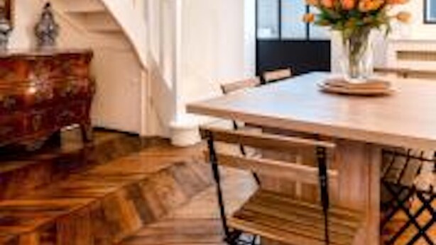A dining area with a wooden table, chairs, a vase of flowers, and a staircase. - Eiffel Tower Lourmel Residence  (Paris)