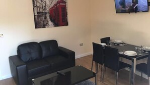 A living room with a black sofa, a glass coffee table, a dining table with chairs, and a flat-screen TV mounted on the wall. - North Crescent (Leeds)