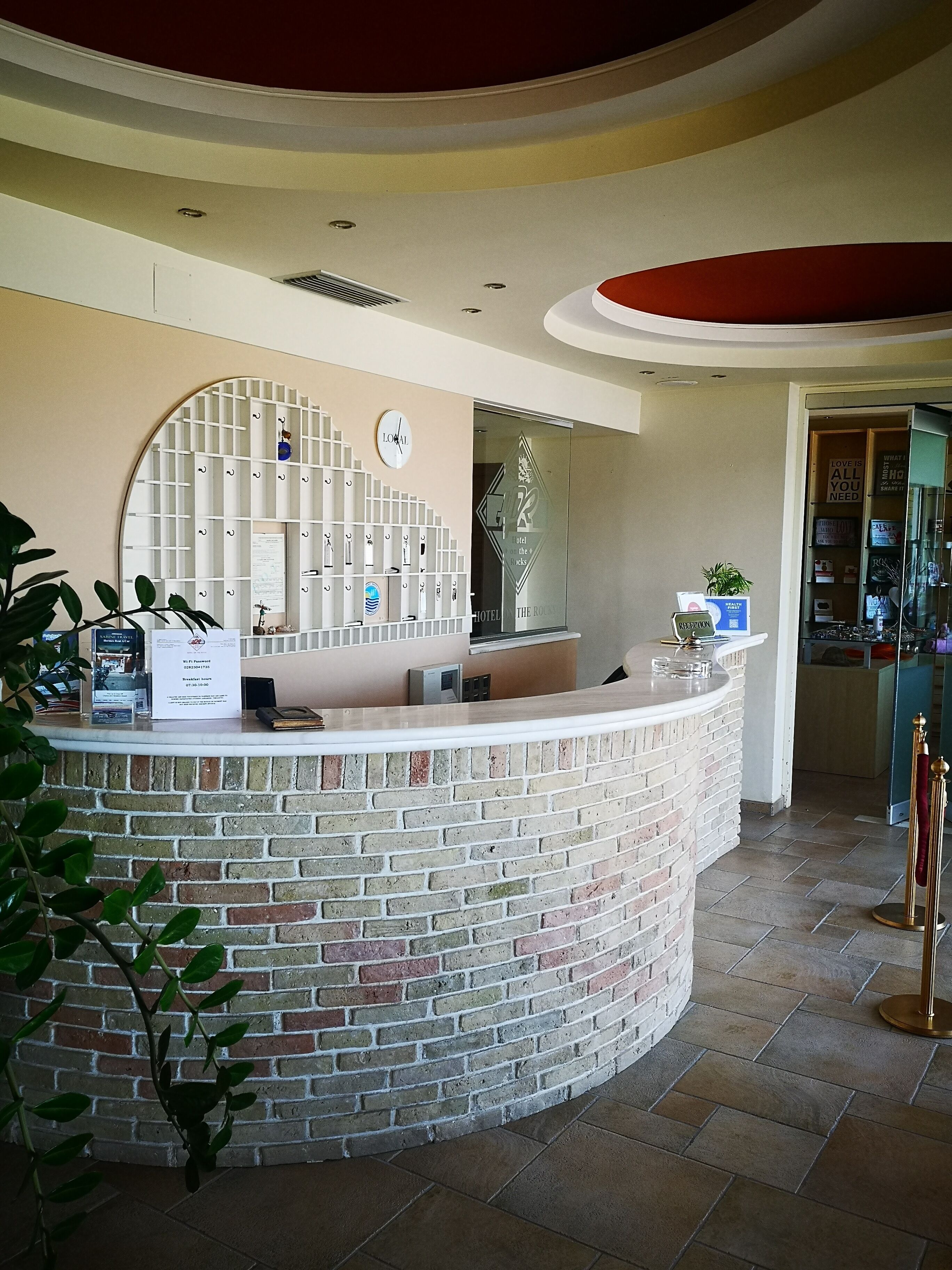 A reception desk with a brick facade, a clock, and a glass door leading to a lobby area.