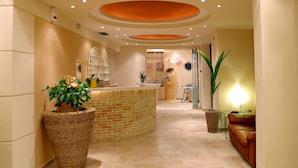 A reception area with a brick counter, wicker planters, a glass table, and a leather sofa. - Hotel On The Rocks (Kantanos-Selino)
